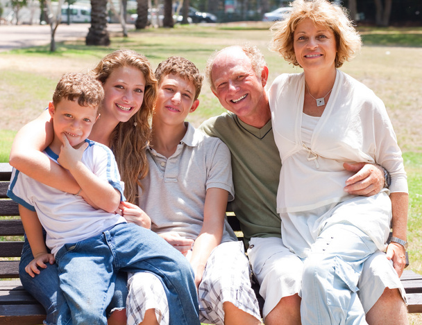Onnellinen perhe istuu puistossa penkillä
 - Valokuva, kuva