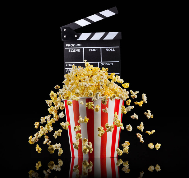 Flying popcorn and film clapper board isolated on black background - Foto, afbeelding