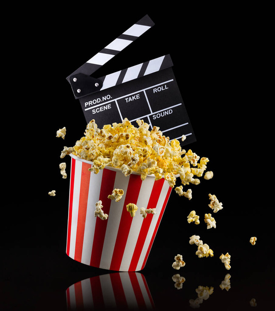 Vliegende popcorn en film clapper board geïsoleerd op zwarte achtergrond, concept van tv-kijken of bioscoop. - Foto, afbeelding