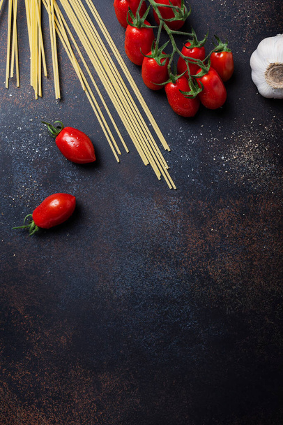 Ingredients for cooking italian pasta: spaghetti, tomato and garlic on the black table. Top view image with a copy space - Foto, immagini