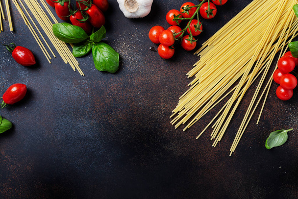 Υλικά για το μαγείρεμα ιταλικών ζυμαρικών: μακαρόνια, ντομάτα, βασιλικό και σκόρδο στο μαύρο τραπέζι. Εικόνα πάνω προβολής με χώρο αντιγραφής - Φωτογραφία, εικόνα