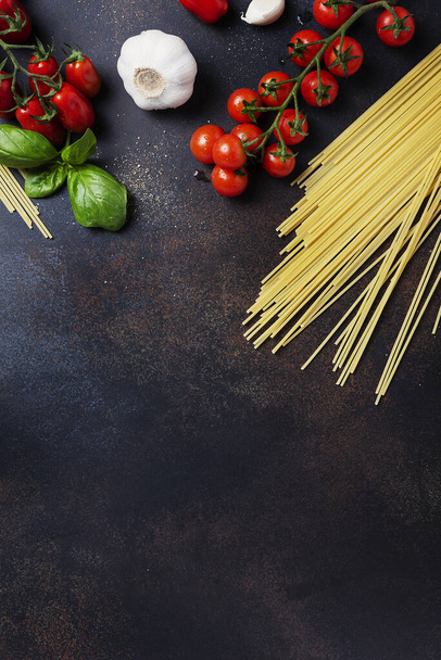Ingredients for cooking italian pasta: spaghetti, tomato, basil and garlic on the black table. Top view image with a copy space - Foto, afbeelding