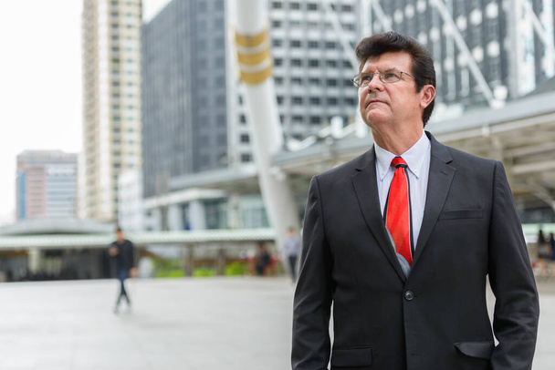 Portrait of mature handsome businessman wearing suit in the city outdoors - Foto, Imagen
