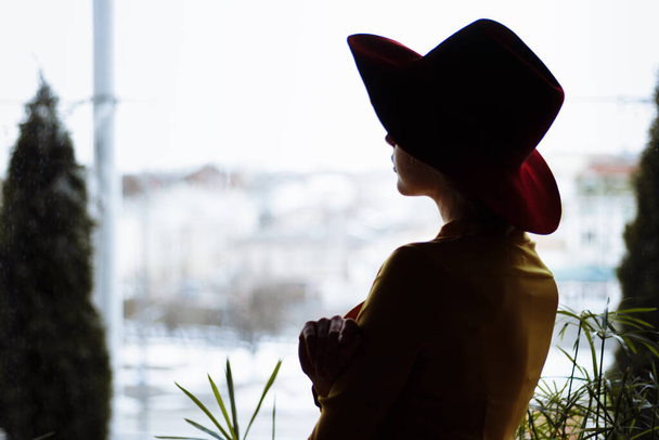 girl in a dress and a hat looks out the window, sad, self-isolation, depression, pandemic, virus - 写真・画像