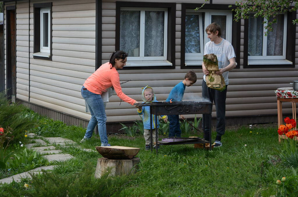 Dad and mom cook a barbecue with their two young sons in isolation in the fresh air at the dacha. - 写真・画像