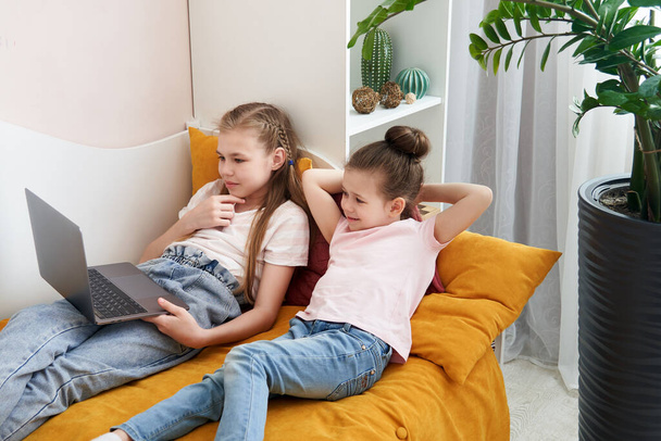 Two little sisters using laptop lying on bed at home - Valokuva, kuva