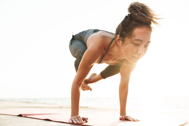 Foto de deportista de fitness en chándal de pie mientras practica yoga junto al mar por la mañana
 - Foto, Imagen