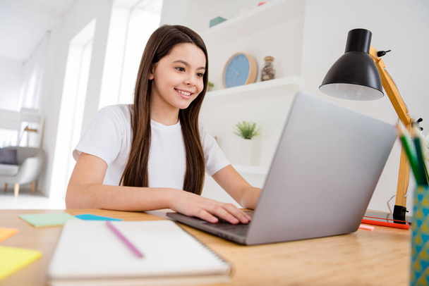 小さなかわいい生徒の学校の女の子のノートパソコンのノートパソコンのオンラインレッスンビデオ通話会議座って机の距離隔離研究宿題快適なリビングルームの教室屋内 - 写真・画像
