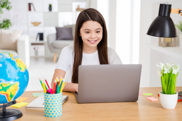 Photo of little pretty pupil small school lady turn on skype laptop notebook online lesson video call sitting table desk distance quarantine study comfort living room classroom indoors - 写真・画像