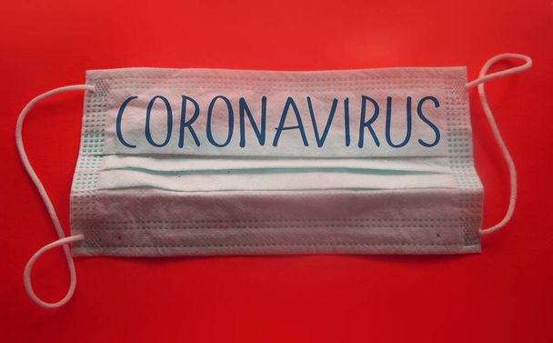 Maska twarzy ze słowem CORONAVIRUS na czerwonym tle. Napis na medycznej masce ochronnej. Epidemia koronawirusa COVID 19, koncepcja medycznego wirusa nCoV. - Zdjęcie, obraz