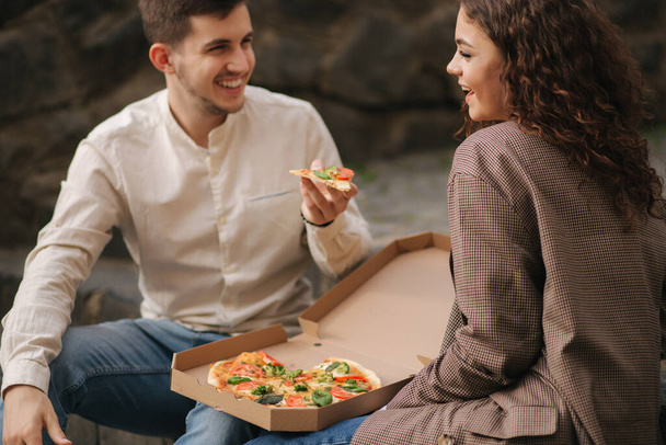 Χαμογελώντας ζευγάρι αγάπη τρώει πίτσα vegan στο δρόμο στις σκάλες. Όμορφος άντρας, δώσε πίτσα στη γυναίκα. - Φωτογραφία, εικόνα