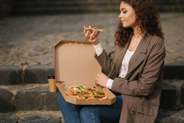 Mulher atraente caixa de pizza aberta e comer pizza vegan ao ar livre
 - Foto, Imagem