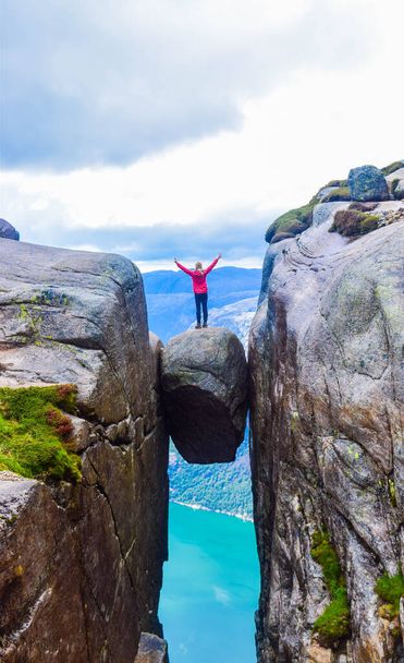A turista lány, aki Kjeragbolten tetején áll - a világ legveszélyesebb köve. A Kjeragbolten egy 984 méter magasságban ragadt szikla Lysefjorden felett a Kjerag hegyen, Norvégiában.. - Fotó, kép