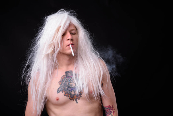 Studio shot of rebellious man as punk rocker wearing wig shirtless against black background - Foto, afbeelding