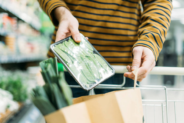 Man in the vegetable department at supermarket puts green been in paper bag - Foto, Imagen
