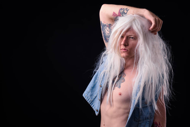 Studio shot of rebellious man as punk rocker wearing wig shirtless against black background - 写真・画像
