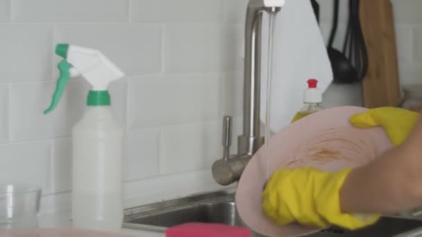 Mujer joven con guantes lavando platos en la cocina
 - Imágenes, Vídeo