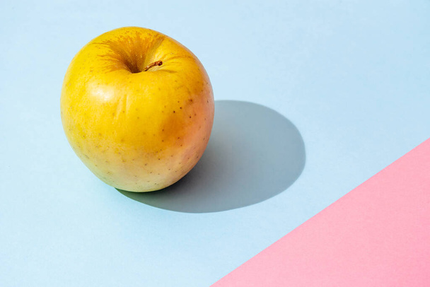 Жовте яблуко на рожево-блакитному фоні з твердою тінь
 - Фото, зображення