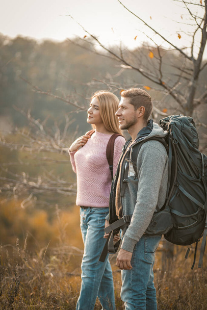 Couple of tourists admiring the natural scenery standing on a mountain side. Side view of a man and woman with backpacks are hiking in nature - 写真・画像