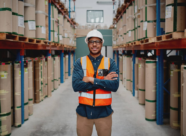 Successful manufacturing unit worker standing in warehouse distribution centre with folded hands with helmet and uniform smiling - Valokuva, kuva