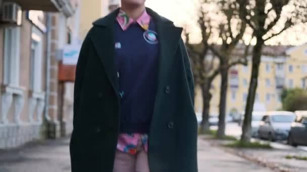 Una joven mujer inteligente con un corte de pelo corto y teñido de pelo, con un abrigo verde y un suéter con estampados en la calle de la ciudad
. - Metraje, vídeo