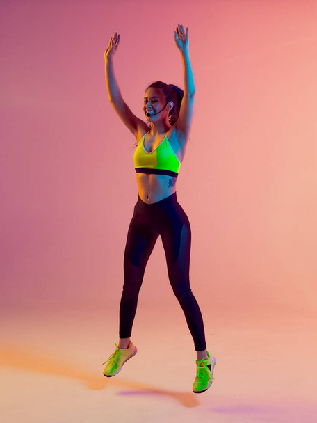 Athletic cool girl trainer teaches group crossfit and work out online training on a bright neon background. - Zdjęcie, obraz