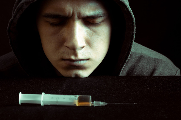 Grunge image of a depressed drug addict looking at a syringe and drugs - Foto, Bild