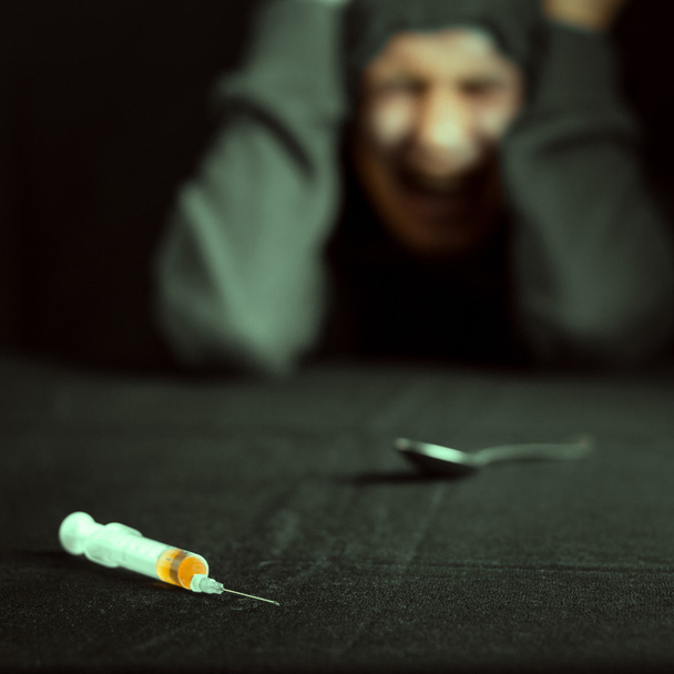 Grunge image of a depressed drug addict looking at a syringe and drugs - Photo, image