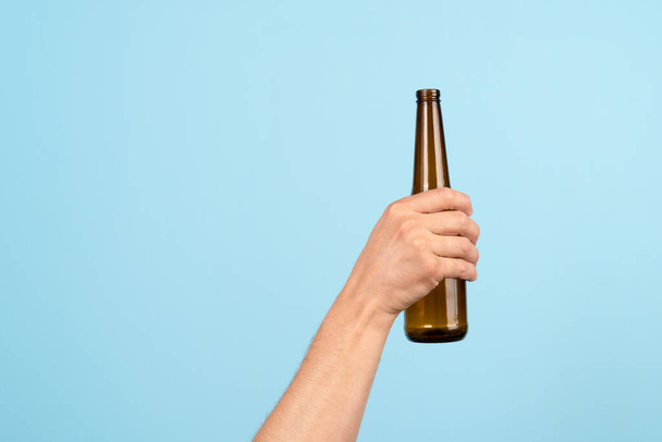 A mão segura uma garrafa de cerveja de vidro vazia em um fundo azul. Ativista cuidar do meio ambiente, triagem de resíduos alimentares para reciclagem adequada bin.Concept de Reciclagem e ecologia
 - Foto, Imagem