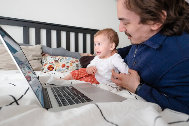 Hombre tratando de trabajar a través de ordenador portátil en casa durante la cuarentena con el bebé. Vida familiar durante el aislamiento personal. Quédate en casa. Trabajo desde casa, oficina en casa
 - Foto, imagen