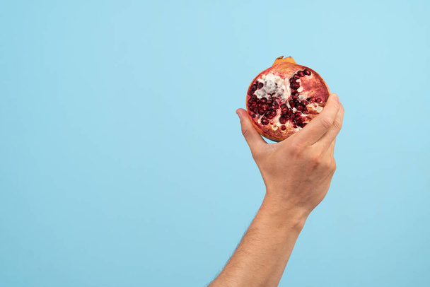 A hand holds a rotten pomegranate organic trash on a blue background. Activist taking care of environment, sorting food waste to proper recycling bin. Concept of Recycling and ecology - Фото, зображення