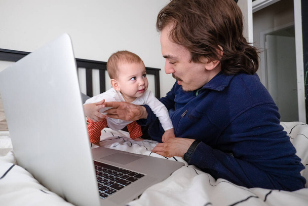 Egy férfi, aki laptoppal próbál dolgozni otthon a karantén alatt a csecsemővel. Családi élet az elszigeteltség alatt. Maradj otthon. Otthoni munka, otthoni iroda - Fotó, kép