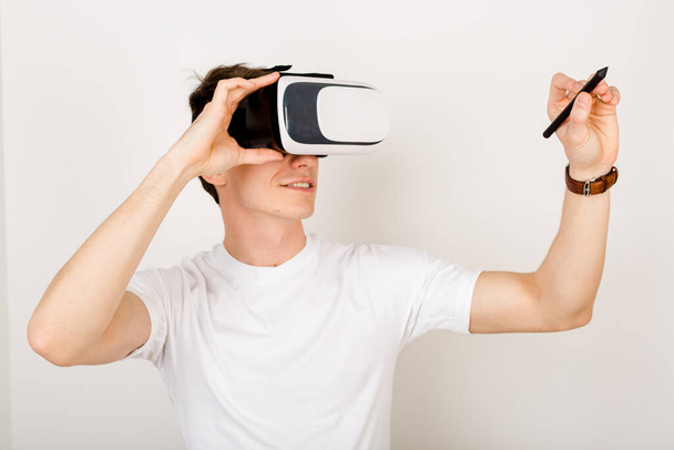 Young man biophysicist using virtual reality headset interacts with augmented things orienting in three dimensional space while sitting on his desk with keyboard and laptop on white background.  - Photo, Image