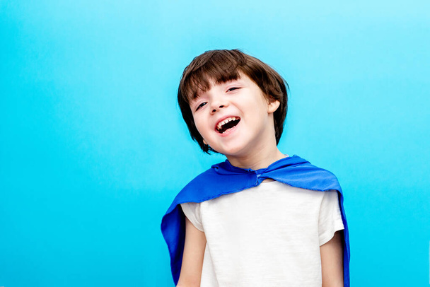 Αγόρι με κάπα υπερήρωα χαμογελά στον ουρανό φόντο, ευτυχισμένη παιδική ηλικία - Φωτογραφία, εικόνα