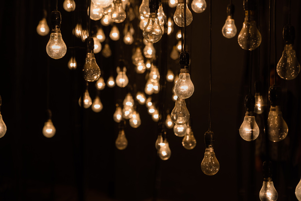 Lit lámparas eléctricas de tungsteno colgando e iluminando un fondo oscuro, instalación de arte abstracto
 - Foto, Imagen