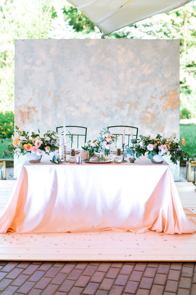 Overall layout of newlyweds groom and bride central table at an open-air tent wedding. welcome dinner on nature background. Pastel design, white illumination of flower arrangements and candlesticks. - Photo, Image
