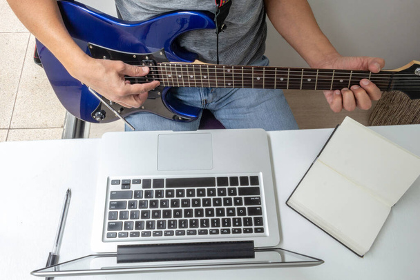 Luchtopname van het detail van handen op een elektrische gitaar en een laptop tijdens een virtuele les. Activiteiten tijdens quarantaine - Foto, afbeelding