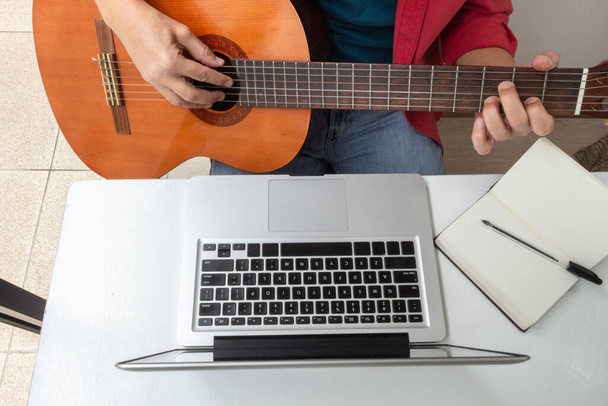 Zdjęcie lotnicze detalu rąk na gitarze klasycznej i laptopie podczas wirtualnej klasy. Działania podczas kwarantanny - Zdjęcie, obraz