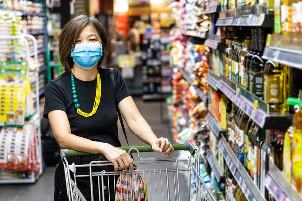 Asijské žena nakupování potraviny v supermarketu s ochrannou maskou obličeje jako nový normální požadavek v Malajsii - Fotografie, Obrázek
