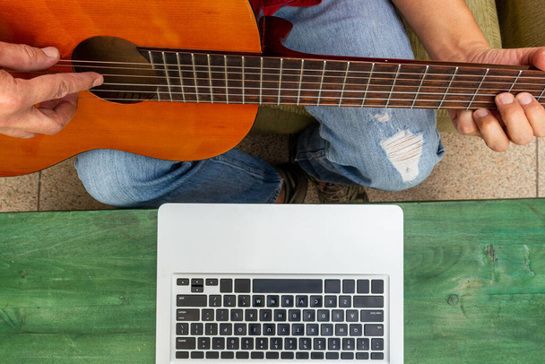 Zenit-Aufnahme der Taille eines Menschen vor seinem Computer, der von zu Hause online Gitarrenunterricht erhält - Foto, Bild