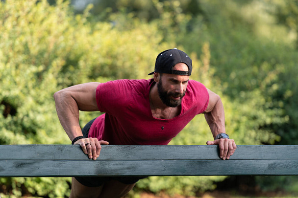 Handsome Young Man in a Red T-shirt Pushups on a Park Bench - Photo, Image