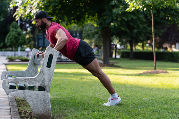 Young Man in Red T-shirt Working Out Doing Push-ups on a Wooden Park Bench as He Warms Up for His Daily Workout or Jog - Fotó, kép