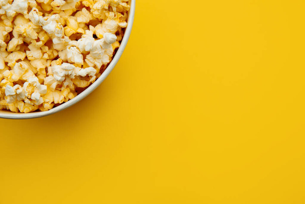 Popcorn in a bowl on yellow background, top view. Entetainement concept - Zdjęcie, obraz