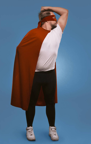 Super hero man ready to save world. Serious man shows and kisses his muscles standing in red super hero mask and coat. Cut out on faded denim blue background - Photo, Image