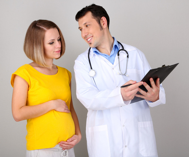 Young pregnant woman with doctor on gray background - Foto, Bild