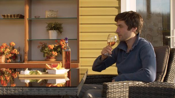 Young man drinking wine. Family celebration outdoors. Cheese, fruits and nuts on the table outdoors. Spring, the evening sun shining on the glass. - Fotoğraf, Görsel