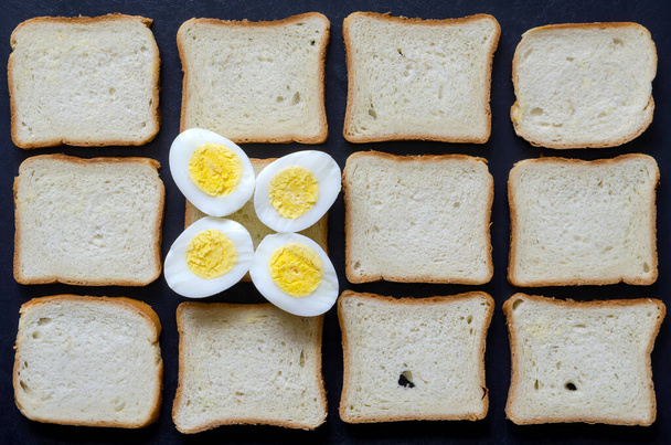 Kreativní zázemí s vařenými vejci a toastovým chlebem. Dvě vejce rozříznutá vejpůl na podkladě kousků chleba. Víceúčelové pozadí. Místo pro text. Pohled shora. - Fotografie, Obrázek