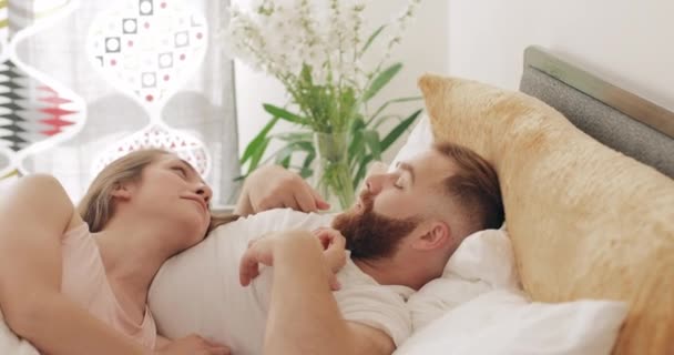 Good looking man and woman communicating and smiling while lying on bed. Loving young couple talking to each other and having good time in morning. Concept of happy relationship. - Video