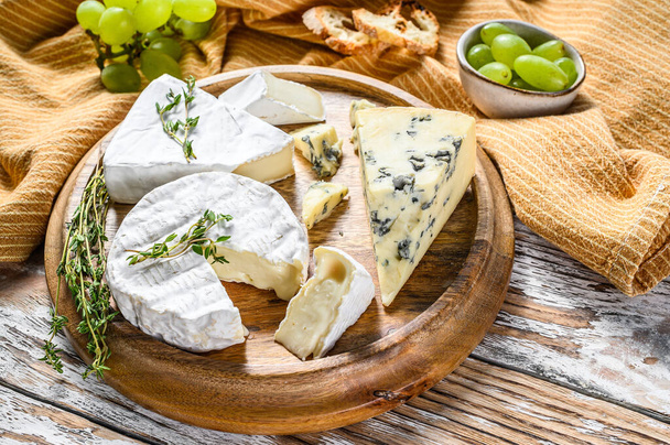 Käseteller mit Camembert, Brie und Blauschimmelkäse mit Trauben. Weißer Holzhintergrund. Ansicht von oben. - Foto, Bild