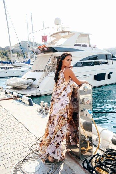 fashion outdoor photo of beautiful woman with dark hair in elegant dress posing in dock with yachts - Фото, изображение